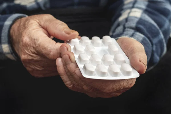 An elderly man holds pills in a blister pack in his hands. Taking pills to treat the disease