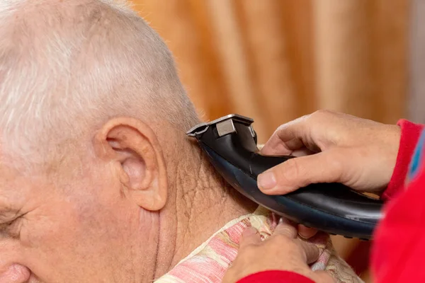 stock image Haircut of an elderly man at home. A woman cuts an elderly man's hair with a trimmer