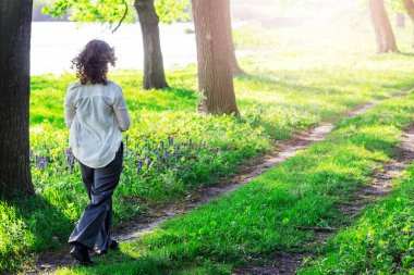 Genç bir kız güneşli yaz havasında bir nehrin yanında orman yolu boyunca yürür. Ormanda bir yürüyüş.