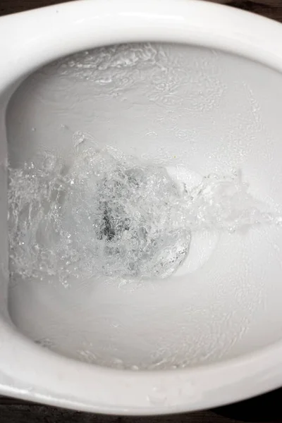 Toilet while flushing urine with water. A stream of water in the toilet bowl
