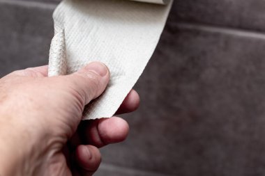 Bir adam tuvalet kağıdını bir rulo kağıttan koparıyor.