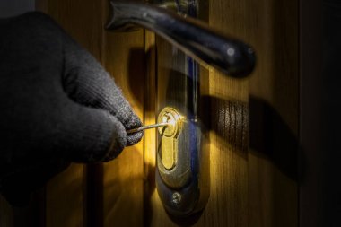 The thief tries to open the lock in the door with a special key clipart