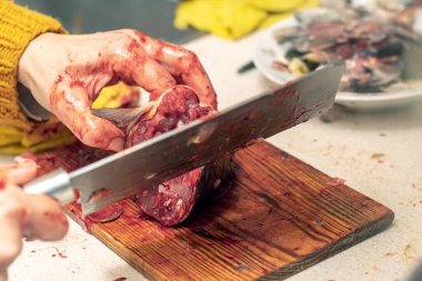 Bir kadın mutfakta büyük bir bıçakla balık kesiyor.