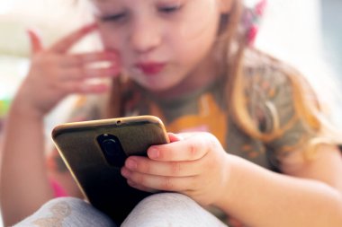 Küçük bir kız dikkatle telefonuna bakıyor. Çocuklar ve modern teknoloji. Telefon bağımlılığı