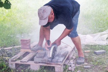 Sokakta çalışan bir işçi güneşli bir yaz gününde kaldırım taşlarını öğütücüyle kesiyor.