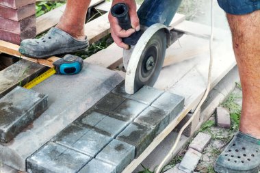 Sokakta çalışan bir işçi güneşli bir yaz gününde kaldırım taşlarını öğütücüyle kesiyor.