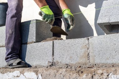İnşaatçı havalandırmalı beton bloklardan yapılmış bir duvar inşa edilirken bir mala tutar.