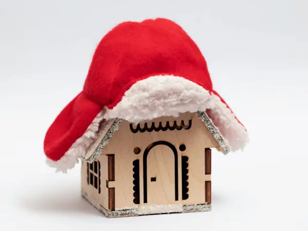 A wooden toy house in the snow is covered with a warm hat. The concept of house insulation and heat preservation