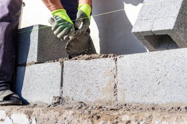 İnşaatçı havalandırmalı beton bloklardan yapılmış bir duvar inşa edilirken bir mala tutar.