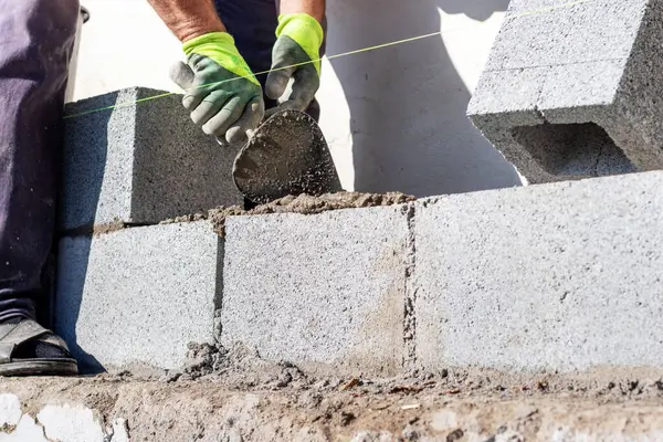 İnşaatçı havalandırmalı beton bloklardan yapılmış bir duvar inşa edilirken bir mala tutar.