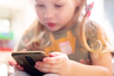 Küçük bir kız dikkatle telefonuna bakıyor. Çocuklar ve modern teknoloji. Telefon bağımlılığı