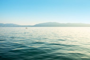 Deniz manzarası: Dalgalı deniz ve mavi gökyüzünün altında uzak bir sahil.