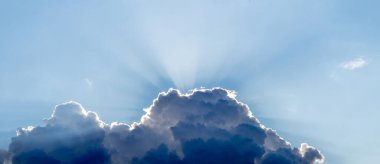 Büyük, siyah kıvrımlı bir bulutun arkasından bakan bir güneş ışığı.