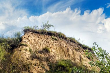 Düşük açılı bir uçurum, bulutlu mavi gökyüzüne karşı bitki örtüsüyle kaplı.