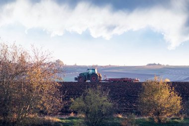 Ukrayna, Khmelnytskyi bölgesi, Ekim 2024. Sonbaharın başlarında traktör engin gökyüzünün altında çalışır kırsal manzaralı bulutlu bir gökyüzü yaratır.