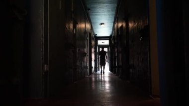 Karanlık bir koridorda ışığa doğru yürüyen birinin arka görüntüsü.