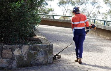 CANBERRA, ACT - 14 MAR 2023: Genç Avustralyalı kadın peyzaj işçisi yerel parkın kenarlarını buduyor.