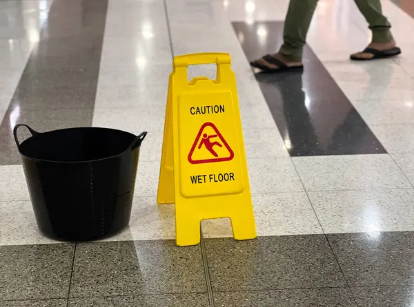 Unrecognizable person passing by a caution wet floor sign and a bucket