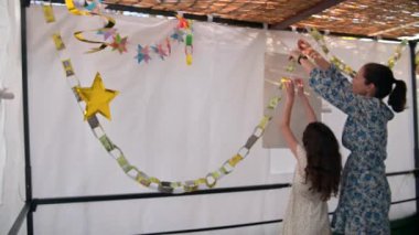 Yahudi anne ve kızı, Sukkot bayramı için geçici bir suka kulübesi dekore ediyorlar..