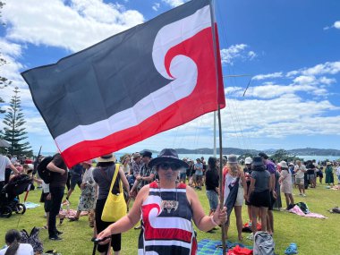 WAITANGI, NZL - FEB 06 2025:Maori people carrying the National Mori flag on Waitagi Day, theFlag representing the Mori people of New Zealand. clipart