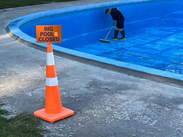 KATIKATI, NZL - MAR 05 2025: Yüzme havuzunu süpürgeyle temizleyen tamirci. Çevre kaynaklarından ve yüzücülerden havuz kirletici maddeler ve rüzgârlı toprak ve enkaz içeriyor.