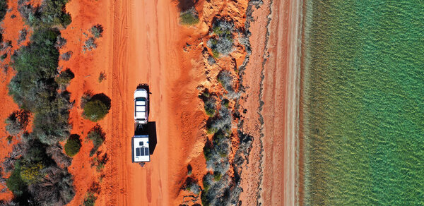 Panoramic aerial landscape view of vehicle towing a caravan on a dirt road along an exotic empty beach at Peron Peninsula in Shark Bay, Western Australia.