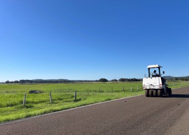 Tanınamayan yol sıkıştırıcı sürücüsü yeni kırsal yol çalışması üzerinde çalışıyor.