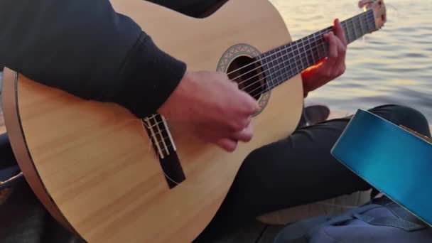 ビーチで座っている間にクラシックギターを弾いているミュージシャンのクローズアップ映像 — ストック動画