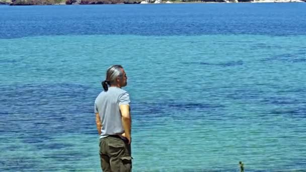 Мужчина Среднего Возраста Длинными Волосами Стоит Пляже Смотрит Морские Кадры — стоковое видео
