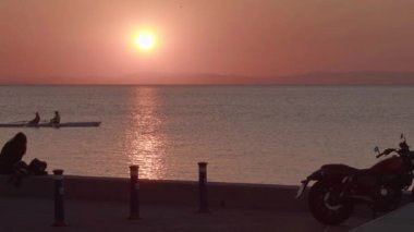 Okyanus kıyısında motosikletli bir kadın Alacakaranlık Kano Sporcularının Hareketli Görüntülerini izliyor..