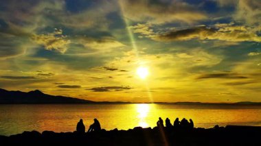 Sunset Video 'da Ocean Beach' te oturan bir grup insan siluetleri..