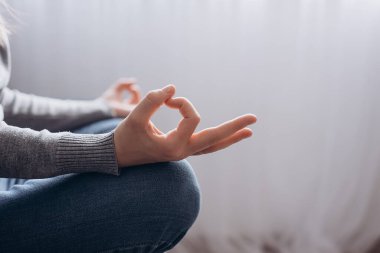 Nilüfer çiçeği pozu ve meditasyonda oturan, evde yoga yapan, el ve el hareketleri yapan, duyguları kontrol eden sakin, stressiz, sağlıklı yaşam tarzı kavramı olmayan, tanınamaz hale gelmiş genç bir kadının yakın çekimi.