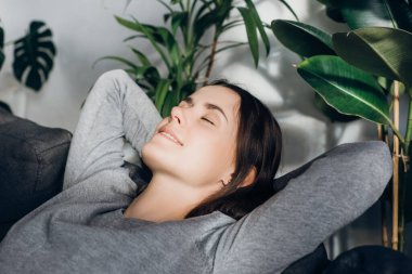 Arkana yaslan ve rahatla. Mutlu, genç ve güzel bir kadının yüz ifadesiyle rahat bir kanepede tek başına. Portre rahatlamış gülümseyen beyaz kadın evinde dinleniyor.