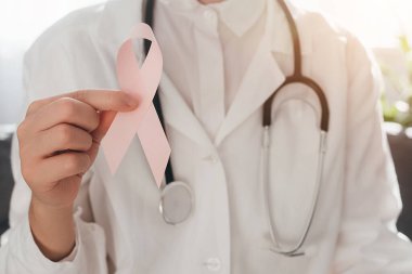 Doktor kadının elinde yaşayan ve hasta insanları desteklemek için küçük pembe bir kurdele tutmasına yakın çekim. Sağlık, Uluslararası Kadınlar Günü ve Dünya Kanser Günü konsepti. Ekim Göğüs Kanseri Farkındalığı Ayı