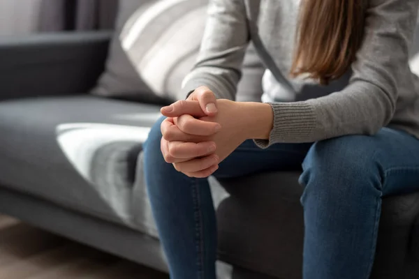 Close up of unrecognizable young woman folded hands together, sit on couch alone, upset desperate female thinking about life, health or emotional problem, feeling sad, suffering from anxiety concept