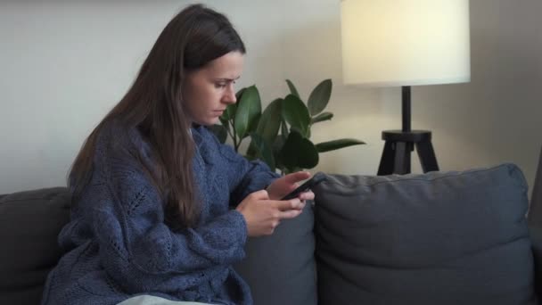 Σοβαρή Στοχαστική Νεαρή Γυναίκα Κάθεται Στον Καναπέ Κρατώντας Συσκευή Smartphone — Αρχείο Βίντεο