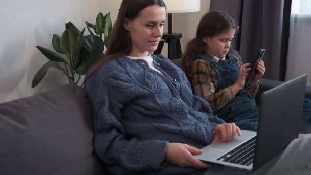 现代技术概念 快乐的年轻妈妈和可爱的微笑的小女儿 用不同的小玩意 在网上玩耍 在家里客厅里舒适的沙发上休息 — 图库视频影像