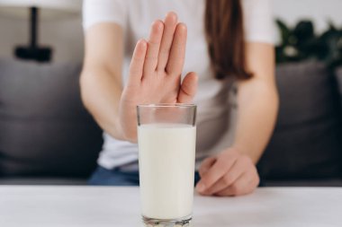 Lactose intolerance concept. Close up of young woman pushing glass of milk deny to drink. Unhealthy girl feels bad, has an upset stomach, bloating due to lactose intolerance. Dairy intolerant person clipart