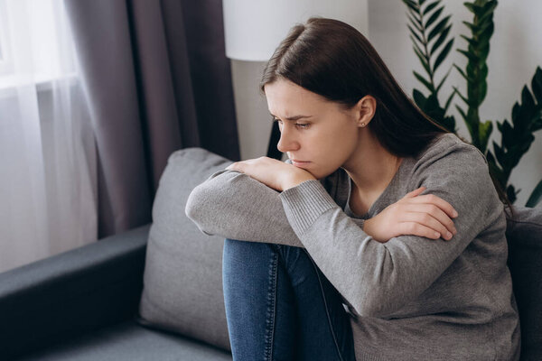 Страшные грустные молодые кавказские женщины 20 лет, сидящие на диване, смотрят вдаль, размышляют или размышляют, имеют личные жизненные проблемы. Задумчивая расстроенная брюнетка беспокоится. Проблема, концепция стресса