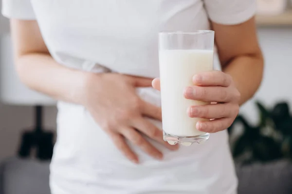 Close up of young caucasian woman with stomach ache and holding glass of milk. Unhealthy female suffers from stale product. Dairy intolerant, Lactose intolerance, allergy, health care concept