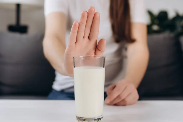 Lactose intolerance concept. Close up of young woman pushing glass of milk deny to drink. Unhealthy girl feels bad, has an upset stomach, bloating due to lactose intolerance. Dairy intolerant person