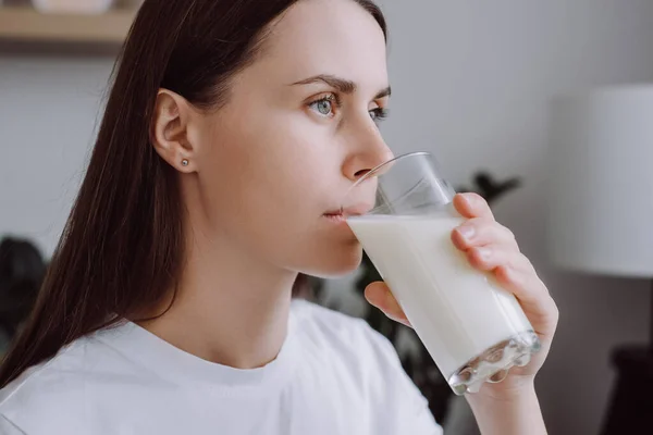 Healthy young brunette woman 20s drinking milk with calcium for strong bone at home, cute lady holding soy milk on glass enjoy with nutrition wellness life. Wellness with natural milk fresh concept