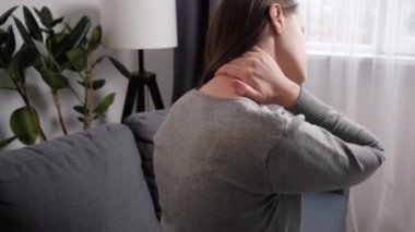 Evde koltukta oturan yorgun, esmer bir kadın. Sert boyun ağrısı, gergin kaslar acı veren duyguları azaltıyor. Omuz ağrısı fibromiyalji osteoartrit bunak kronik hastalıklar konsepti