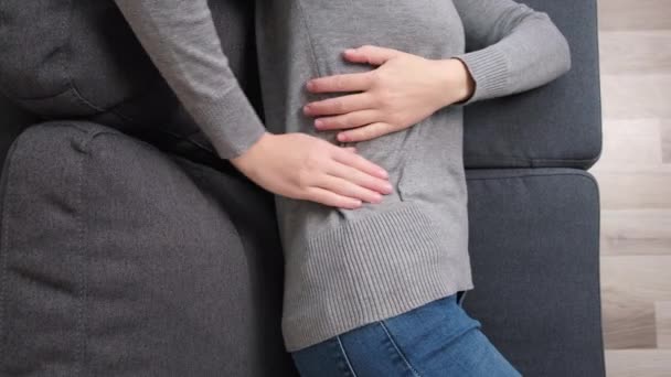 月経痛に苦しむ病気の女性のトップビュー 痛みを伴う胃の痛みやソファの上に横たわる期間けいれんを持つ腹を絞る手を持つ女の子 腹部の痛み 胃炎と痛みを伴う期間の概念 — ストック動画