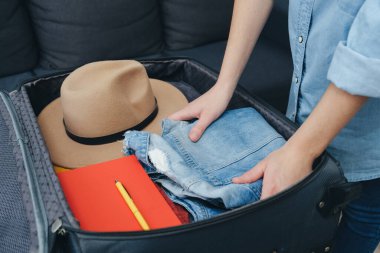 Yolculuk yaşam tarzı kavramı. Bavulları hazırlayan ve düzenleyen kadın elleri. Sıralama ve bagaj paketleme için giysi yığını. Tatile hazırım. Seyahat blogcusunun temel ihtiyaçları
