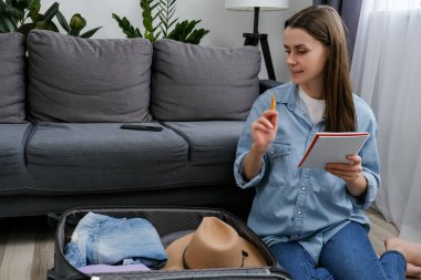 Seyahat konseptinin sırt çantalı seyahati. Sevimli 20 'li yaşlarda genç bir bayan listeyi not alır ve listeyi kontrol eder, bavulları hazırlar ya da bavula yerleştirir, yolculuk için seyahat çantası hazırlar. Seyahat eden, tatilde olan insanlar