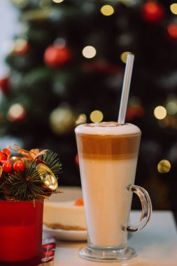 Süslü Noel ağacına karşı beyaz masa üzerinde saman olan bir bardak milkshake 'in dikey görüntüleri. Neşeli içkiler ve mutlu yıllar.