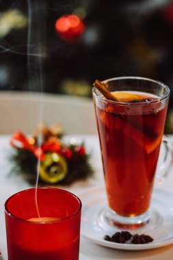 Mum ve Noel 'in dikey görüntüleri arka planda süslenmiş Noel ağacının üzerinde baharatlar ve meyvelerle dolu kırmızı şarabı kaynattı. Geleneksel sıcak içecek. Mutlu yıllar ve tatil konsepti. Seçici odak