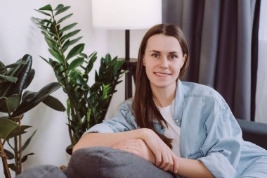 Çekici, genç, esmer bir kadın. 20 'li yaşlarda, mutlu bir şekilde kameraya bakıyor. Hoş, gülümseyen bir kız, oturma odasında rahat koltukta oturuyor.