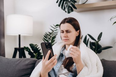 Sosyal uzaklık, koronavirüs konsepti için karantina. Hasta 20 'li yaşlardaki genç bir kızın portresi telefon görüşmesi ile doktor danışmanlığı ya da internet danışmanlığıyla konuşuyor. Oturma odasındaki kanepede oturuyor.